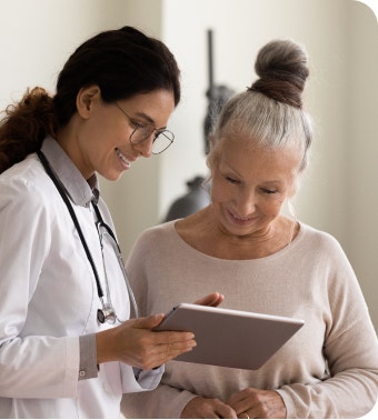 Female doctor and an older female patient reviewing a tablet whilst smiling.