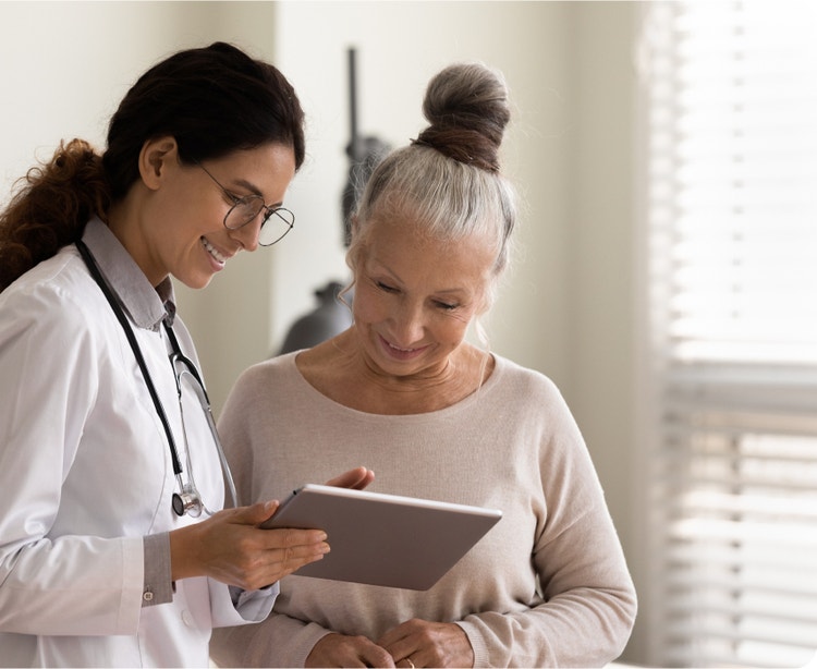 Female doctor and an older female patient reviewing a tablet whilst smiling.